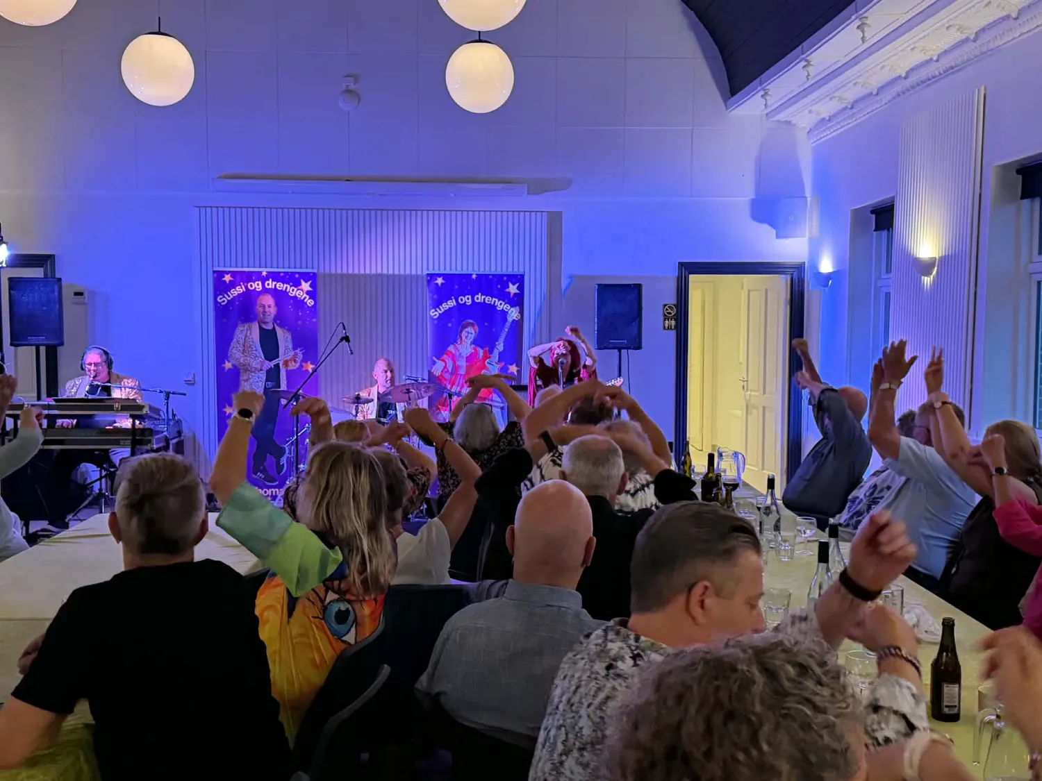 Sussi & Drengene spiller på scenen i Lem forsamlingshus med blåt lys